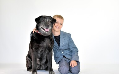 a boy in a suit sits next to a big black dog on a white background