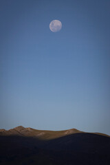  Paisaje andino, cielo azul, luna de fondo, colinas iluminadas tenuemente