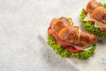 two lye croissant sandwiches with iberian ham, tomato slices, lettuce and cheese on marble board on...