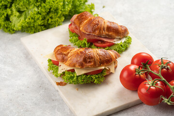 two lye croissant sandwiches with iberian ham, tomato slices, lettuce and cheese on marble board on grey background