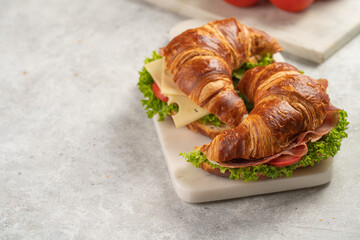 two lye croissant sandwiches with iberian ham, tomato slices, lettuce and cheese on marble board on grey background