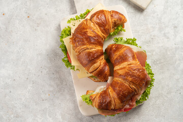 two lye croissant sandwiches with iberian ham, tomato slices, lettuce and cheese on marble board on grey background