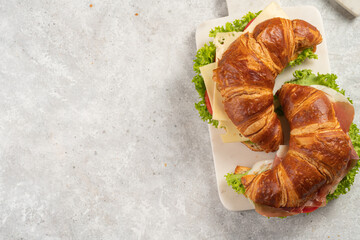 two lye croissant sandwiches with iberian ham, tomato slices, lettuce and cheese on marble board on grey background, space for text