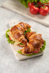 two lye croissant sandwiches with iberian ham, tomato slices, lettuce and cheese on marble board on...