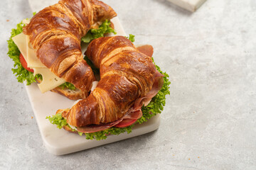two lye croissant sandwiches with iberian ham, tomato slices, lettuce and cheese on marble board on grey background