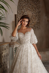 Fashion Beautiful Bride in wedding luxury dress with lace and crystals at arabian style interior. Portrait of Brunette happy woman wears bridal white dress with wedding makeup and hairstyle. Newlywed