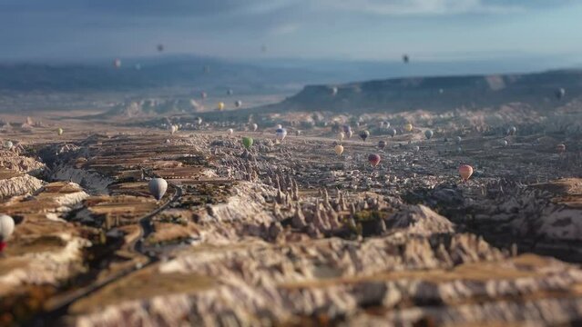 Miniature of limestone valley in Cappadocia and levitating hot air balloons in summer sky. Drone tilt shift footage of plenty flying vehicles with baskets over cone mountains in Turkey. Travel concept