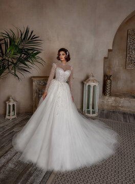 Fashion Beautiful Bride in wedding luxury dress with lace and crystals at arabian style interior. Portrait of Brunette happy woman wears bridal white dress with wedding makeup and hairstyle. Newlywed