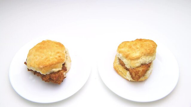 Macro closeup of woman man hands holding placing fresh fast food deep fried chicken meat biscuit crispy sandwich isolated on two white background kitchen table plates