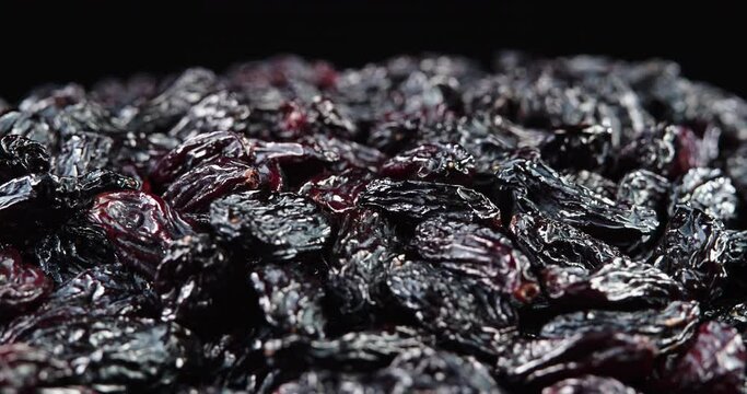 Raisins on black background. A dry grapes macro shot close-up shot. Raisins rotate slowly, close-up. Black raisins, healthy food concept.