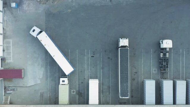 Aerial top down view of a semi-trailer truck driving up to a warehouse ramp for unloading and loading goods in a logistics park