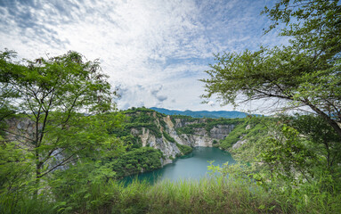 The water in the pond is emerald green surrounded by limestone mountains, big trees and clear sky in Grand Canyon Chonburi, Thailand.