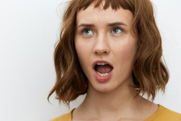 a surprised, shocked woman in a yellow T-shirt stands on a white background and looks up with her mouth wide open. Horizontal Studio Photography