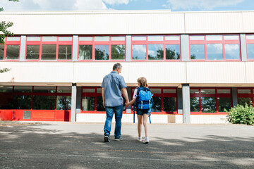 View from the back to dad with a child, holding hands and going to school. Parents accompany their...