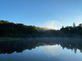 Paysage calme d'une forêt et de l'eau d'une rivière à l'aube. Reflet d'une montagne sur un lac au petit matin. Lever de soleil avec brume sur l'eau.
