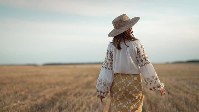 Unrecognizable ethnic woman walking in wheat field after harvesting. Attractive lady in embroidery vyshyvanka blouse and straw hat. Ukraine, independence, freedom, patriot symbol, stylish girl