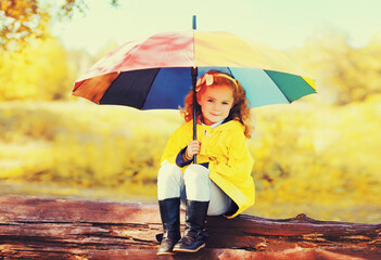 Happy little girl child with colorful umbrella in sunny autumn park