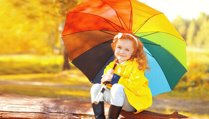 Happy little girl child with colorful umbrella in sunny autumn park