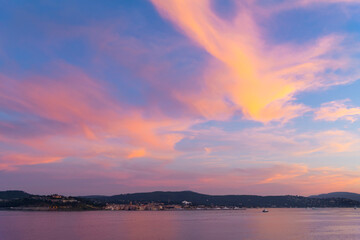 View from a cruise ship at sea of the Castle, port and old town of Saint-Tropez, France, along the Cote d'Azur French Riviera under a colorful sunset sky on the Mediterranean Sea.