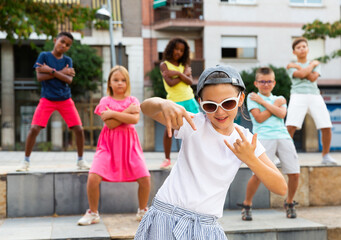 Modern preteen girl krump dancer wearing stylish sunglasses and cap posing during performance with...