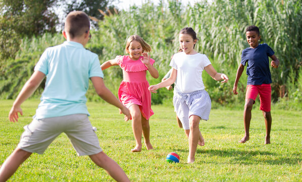 Boys and girls playing football on green grass together outdoors.
