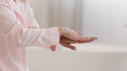 Anti aging skin care. Unrecognizable mature lady rubbing moisturizing cream on hands at home, side view, empty space