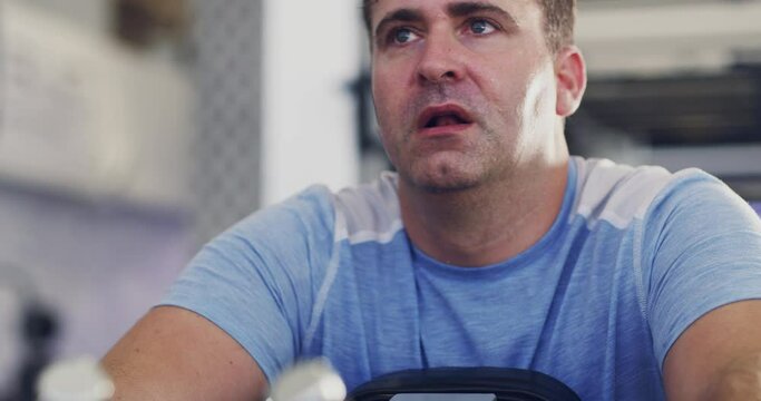 Tired and active man resting after a hard exercise session in a gym. Exhausted man sweating and taking a break from a physical cardio workout to improve health, fitness, weight loss and wellness
