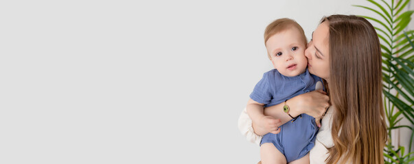 Banner, mockup. Beautiful loving mother in a dress holds her newborn baby boy in a blue suit in her arms. Kisses him on the cheek. Happy loving family