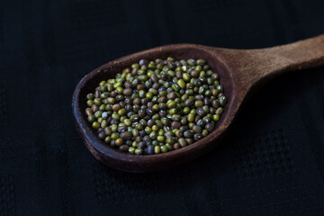 porotos verdes en una cuchara de madera sobre un fondo negro