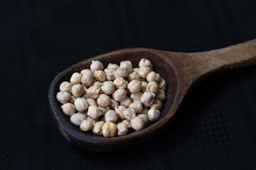 garbanzos crudos en cuchara grande de madera, sobre fondo negro