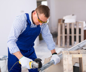 Focused man in protective glasses renovating new home, cutting metal profile using grinding machine