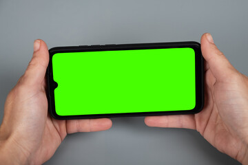 hands holding the phone horizontally, green chroma key mockup on smartphone.