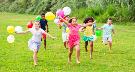 Barefoot children running through field with balloons in hands and smiling.