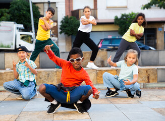 Group of children in casual clothes training hip-hop on street, learning modern dance movements
