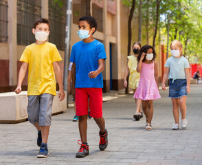 Group of children in protective medical masks walking on city street in fine weather