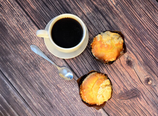 Obraz na płótnie Canvas Two freshly baked cupcakes with sprinkles, a cup of black coffee and a spoon on a wooden table.