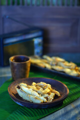 Banana fritters on a wooden plate served with a cup of water on the table with banana leaf