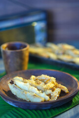 Banana fritters on a wooden plate served with a cup of water on the table with banana leaf