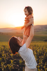 Mom lifted her daughter up, holding in her arms and looking lovingly at the child. Portrait in the corn field. Happy family outdoors. Happy family, childhood