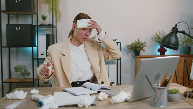 Sick ill businesswoman suffering from cold flu or allergy working on laptop at home office. Manager freelancer girl with towel on head blows sneezes wipes snot into napkin. Coronavirus quarantine