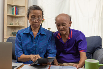 Asian elderly sit and holding calculator for insurance or medical expenses and a computer on desk home.