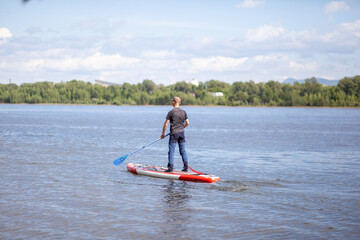 12.07.2022 Krasnoyarsk, Russia. SUP board Stand up paddle man boarding on lake standing happy on blue water. A man swims and rests on a SUP board on the river