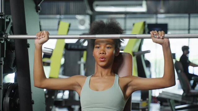 African American sportswoman lift up weight machine or barbell in gym.