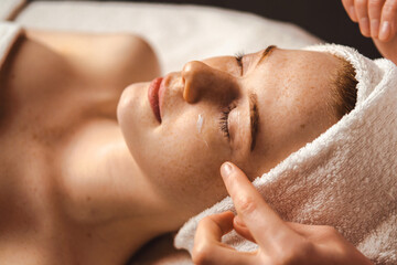 Caucasian freckled woman having face massage in a spa salon. Beauty treatment. Attractive elegant...