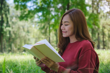 Fototapeta premium Portrait of a beautiful young asian woman reading a book while sitting in the park
