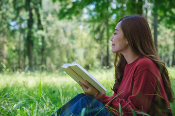 Fototapeta premium Portrait of a beautiful young asian woman reading a book while sitting in the park