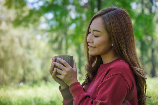 Portrait image of a beautiful young asian woman drinking coffee while sitting in the park