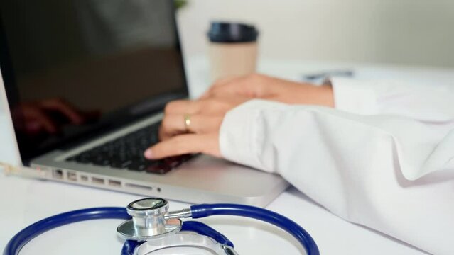 Doctor or nurse woman in uniform with stethoscope working she typing information of patient prescription from paperwork medical history form into laptop computer for record document data report