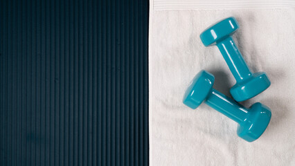 Dumbbells and towel on the workout mat - sports background with space for text