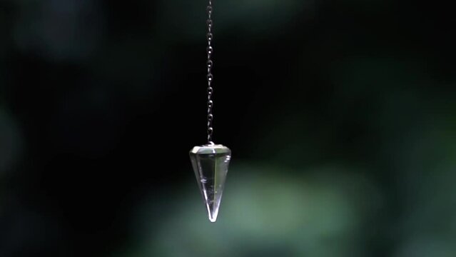 Clear quartz crystal pendulum hanging from Caucasian woman's hands swinging in esoteric and holistic Mystical ritual